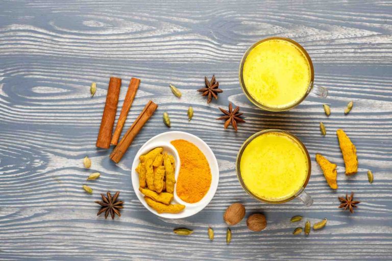 Golden turmeric milk surrounded by spices on a wooden table.