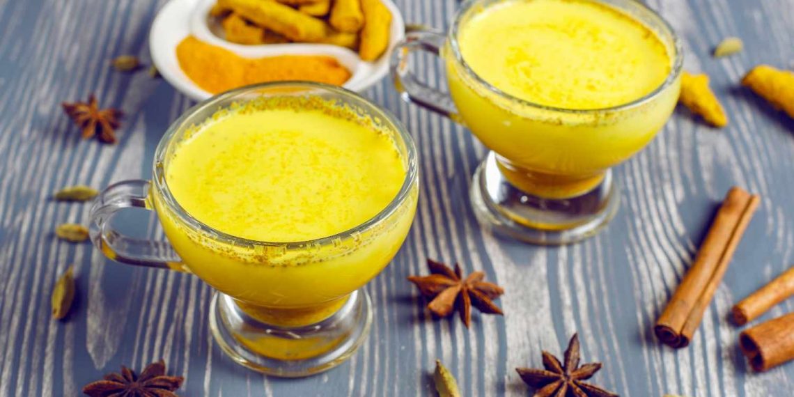 Two cups of turmeric latte with spices on a wooden table.
