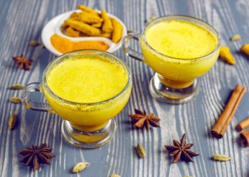 Two cups of turmeric latte with spices on a wooden table.