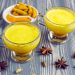 Two cups of turmeric latte with spices on a wooden table.