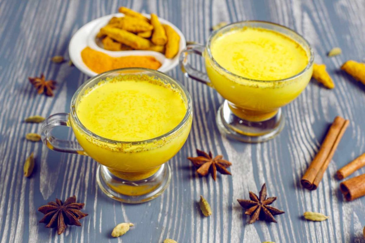 Two cups of turmeric latte with spices on a wooden table.