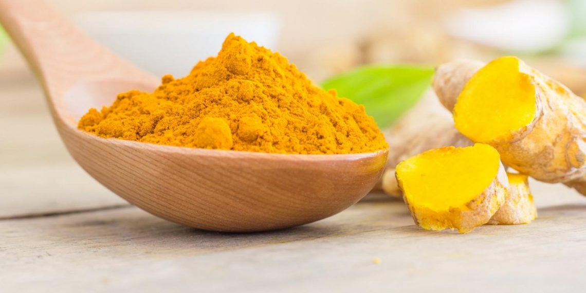 Turmeric powder in wooden spoon on table.