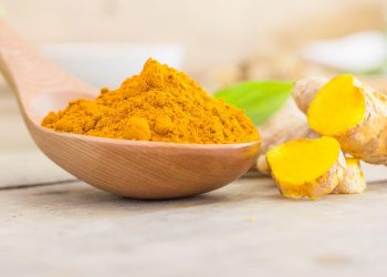 Turmeric powder in wooden spoon on table.