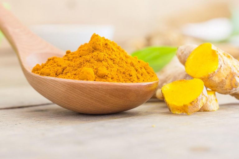 Turmeric powder in wooden spoon on table.