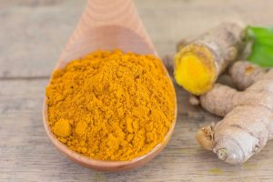 Turmeric powder in a wooden spoon next to fresh turmeric root.