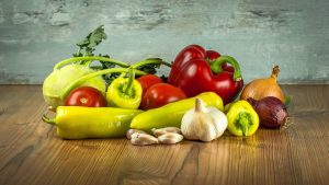 Fresh vegetables on a wooden table including peppers, tomatoes, and garlic.