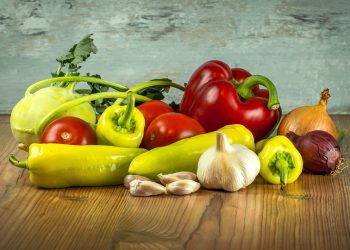 Fresh vegetables on a wooden table including peppers, tomatoes, and garlic.