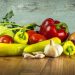 Fresh vegetables on a wooden table including peppers, tomatoes, and garlic.