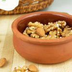 Toasted walnuts and almonds in a clay pot on a wooden board.