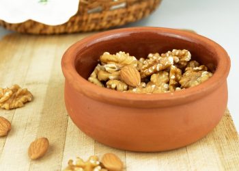 Toasted walnuts and almonds in a clay pot on a wooden board.