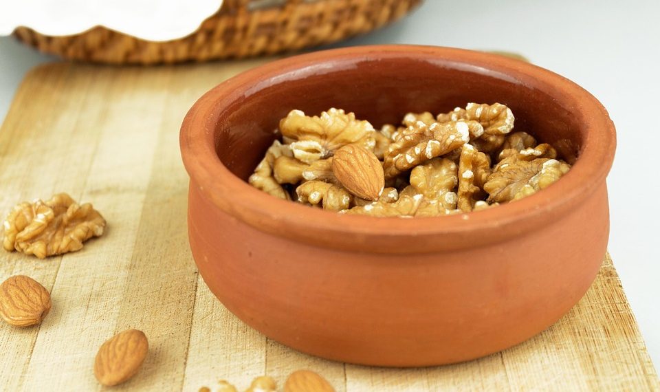 Toasted walnuts and almonds in a clay pot on a wooden board.