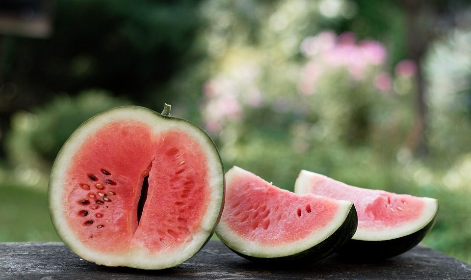 Sliced watermelon on a wooden table outdoors.