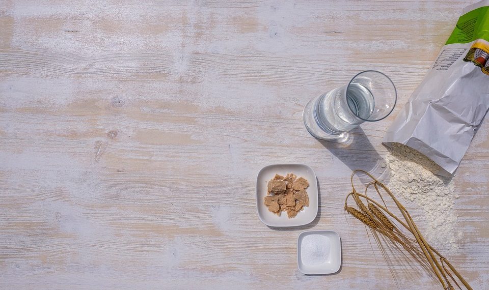 Baking ingredients including flour, yeast, and water on a wooden table.