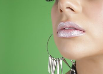 Glossy lips with large hoop earrings against a green background.