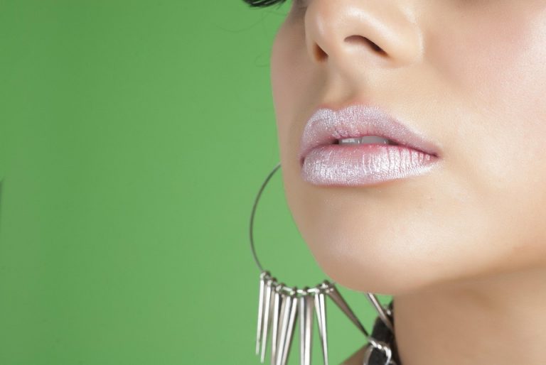 Glossy lips with large hoop earrings against a green background.