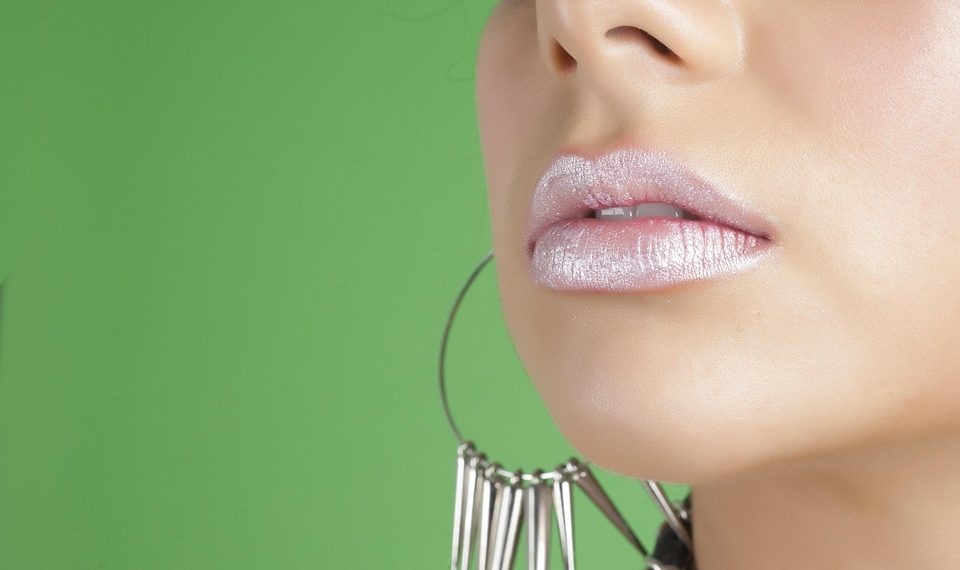 Glossy lips with large hoop earrings against a green background.