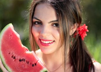 Young woman smiling with a slice of watermelon outdoors.