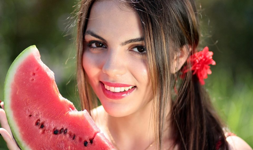 Young woman smiling with a slice of watermelon outdoors.