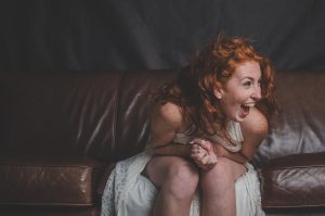 Red-haired woman laughing on a brown leather sofa.