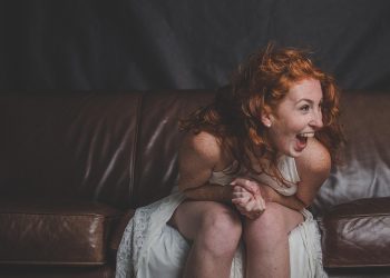Red-haired woman laughing on a brown leather sofa.