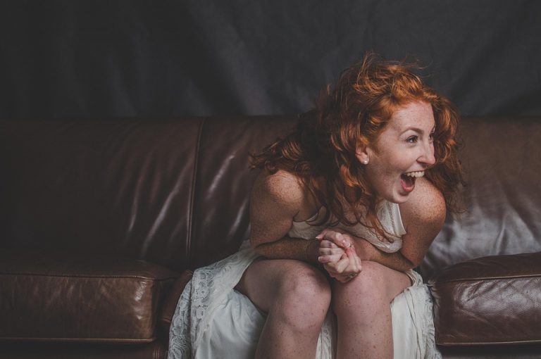 Red-haired woman laughing on a brown leather sofa.