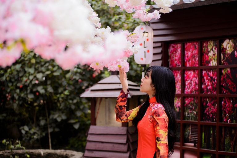 Woman in vibrant dress admiring cherry blossoms indoors.