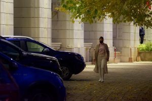 Woman walking past cars on a city street at night.