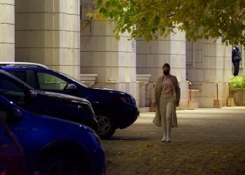Woman walking past cars on a city street at night.