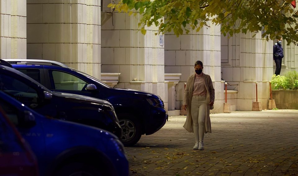 Woman walking past cars on a city street at night.