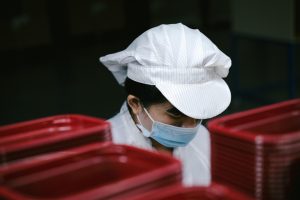 Factory worker wearing a mask and cap near red containers.