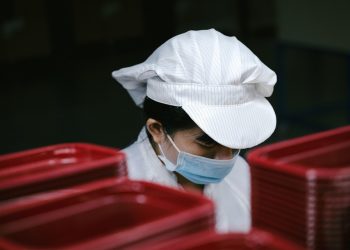 Factory worker wearing a mask and cap near red containers.