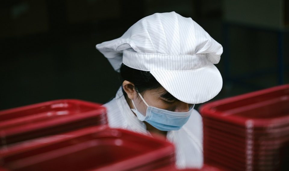 Factory worker wearing a mask and cap near red containers.