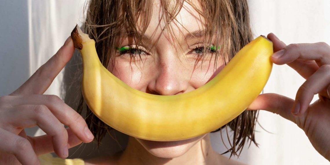 Woman smiling with banana in sunlight.