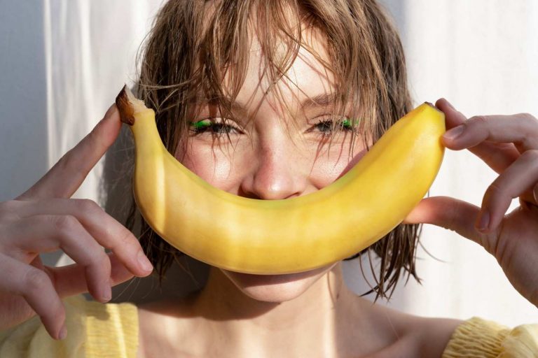 Woman smiling with banana in sunlight.