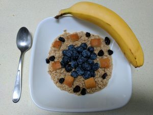 Oatmeal topped with blueberries, apple chunks, raisins, and a banana on the side.
