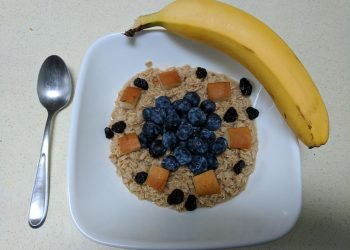 Oatmeal topped with blueberries, apple chunks, raisins, and a banana on the side.