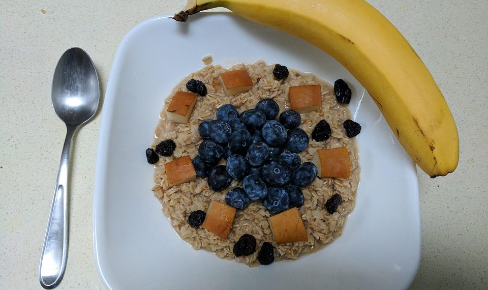 Oatmeal topped with blueberries, apple chunks, raisins, and a banana on the side.