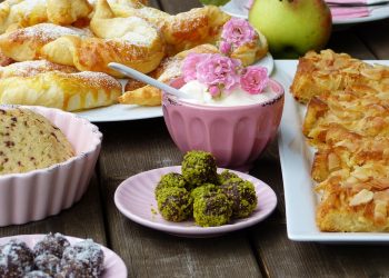 Assorted pastries and desserts with a bowl of cream topped with pink flowers.
