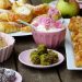 Assorted pastries and desserts with a bowl of cream topped with pink flowers.