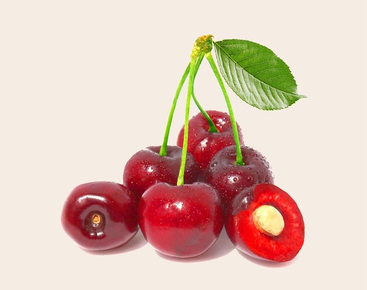 Fresh red cherries with a leaf, one cut open.