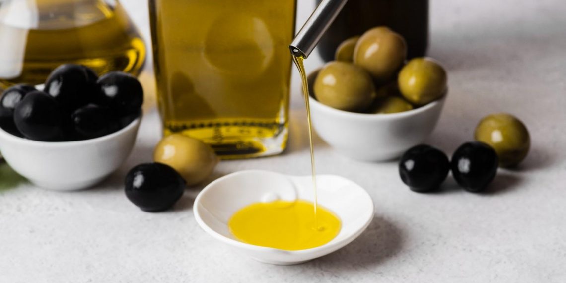 Pouring olive oil into a small dish with black and green olives nearby.