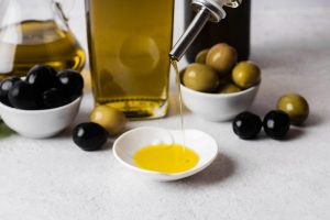 Pouring olive oil into a small dish with black and green olives nearby.