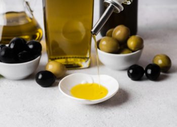 Pouring olive oil into a small dish with black and green olives nearby.