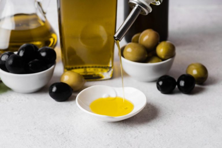 Pouring olive oil into a small dish with black and green olives nearby.