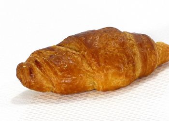 Freshly baked croissant with golden crust on white surface.