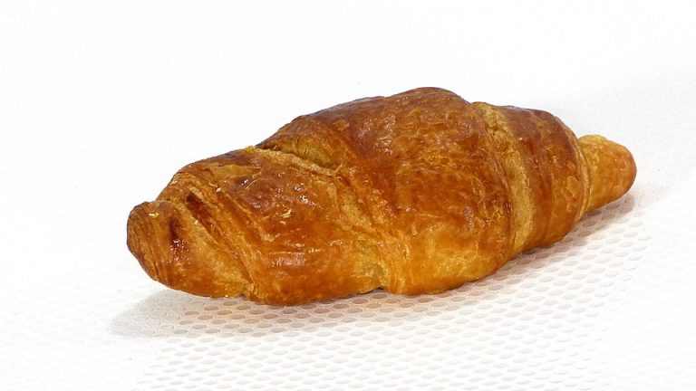 Freshly baked croissant with golden crust on white surface.