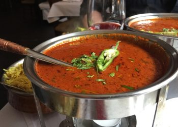 Hot curry served in a metal bowl with garnish of cilantro and chili pepper.