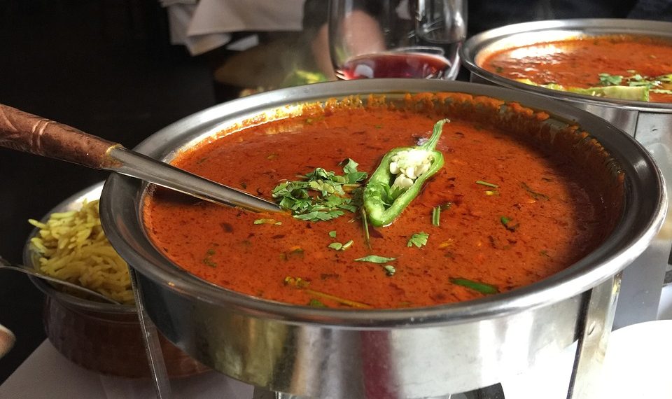 Hot curry served in a metal bowl with garnish of cilantro and chili pepper.