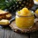 Pineapple jam in a jar with fresh pineapple slices on rustic table.