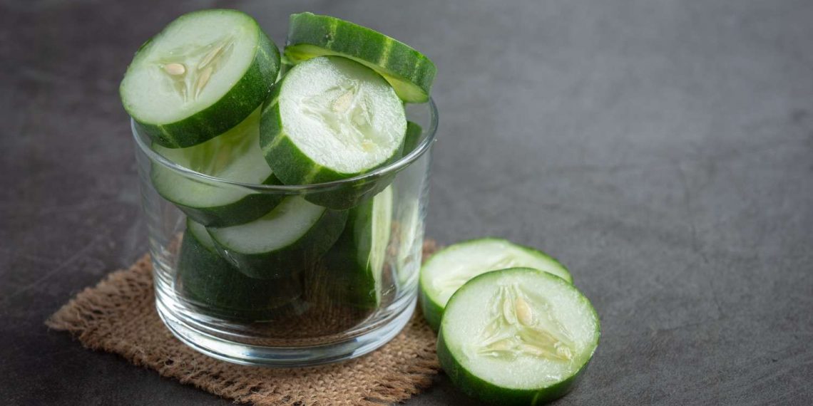 Sliced cucumber slices in a glass bowl on a burlap mat.